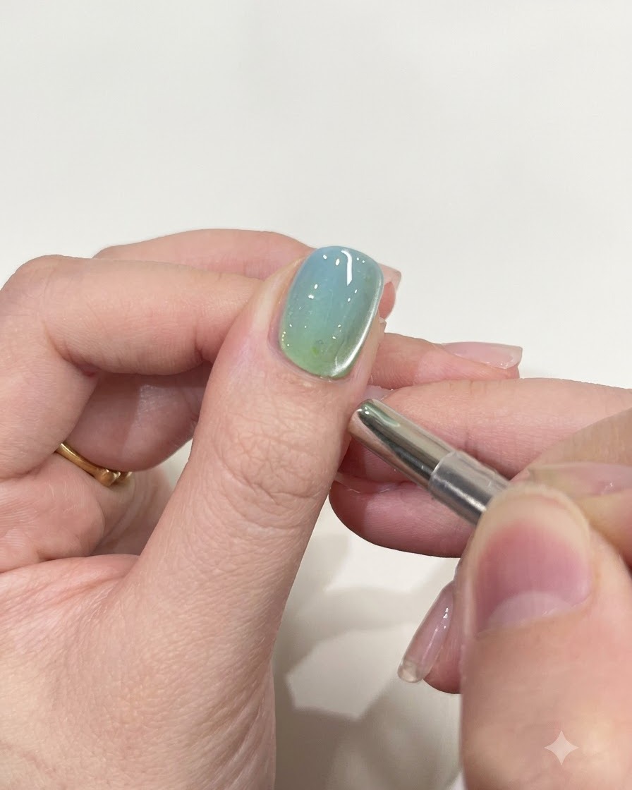 Ein kleines zylindrisches Magnetwerkzeug schwebt nahe am Rand eines glänzend lackierten Nagels.