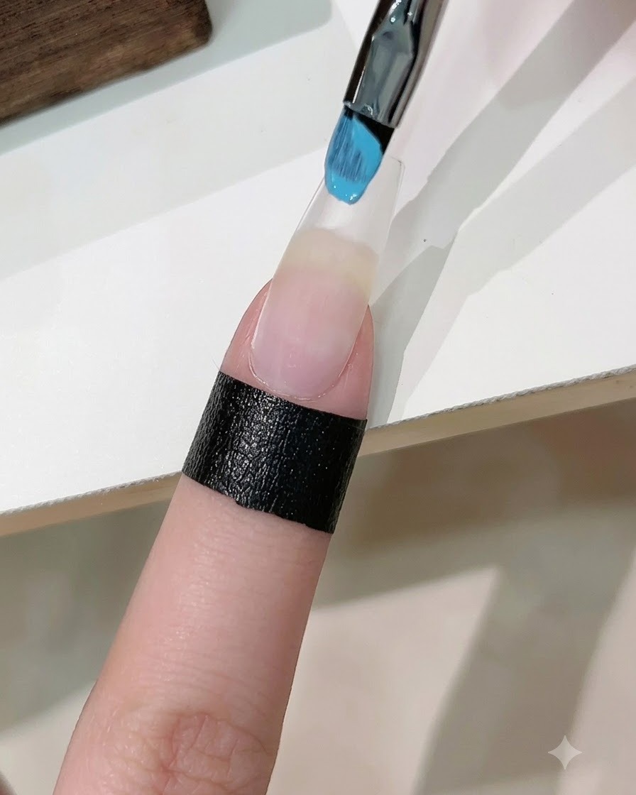 Ein mit blauem und weißem Gel-Nagellack getränktes Schwämmchen tupft einen Farbverlauf auf einen verlängerten Kunstnagel.