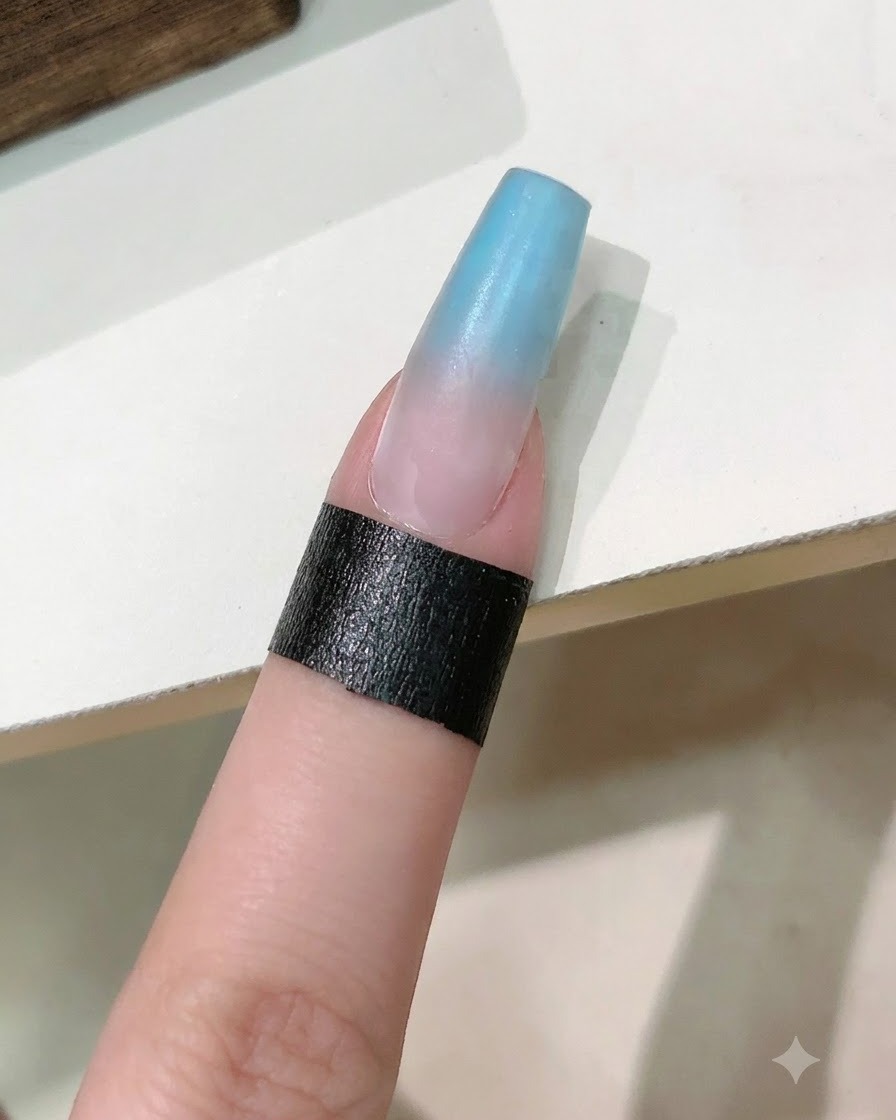 Ein Nagelpinsel trägt eine Schicht klares Aufbaugel über den blau-rosa Farbverlauf-Nagel auf.