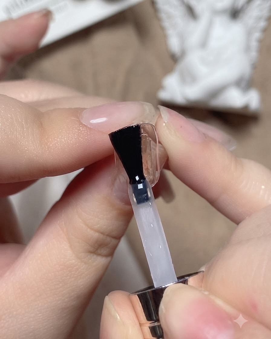 Ein Nagelpinsel trägt einen klaren Base Coat auf einen Übungsnagel auf.