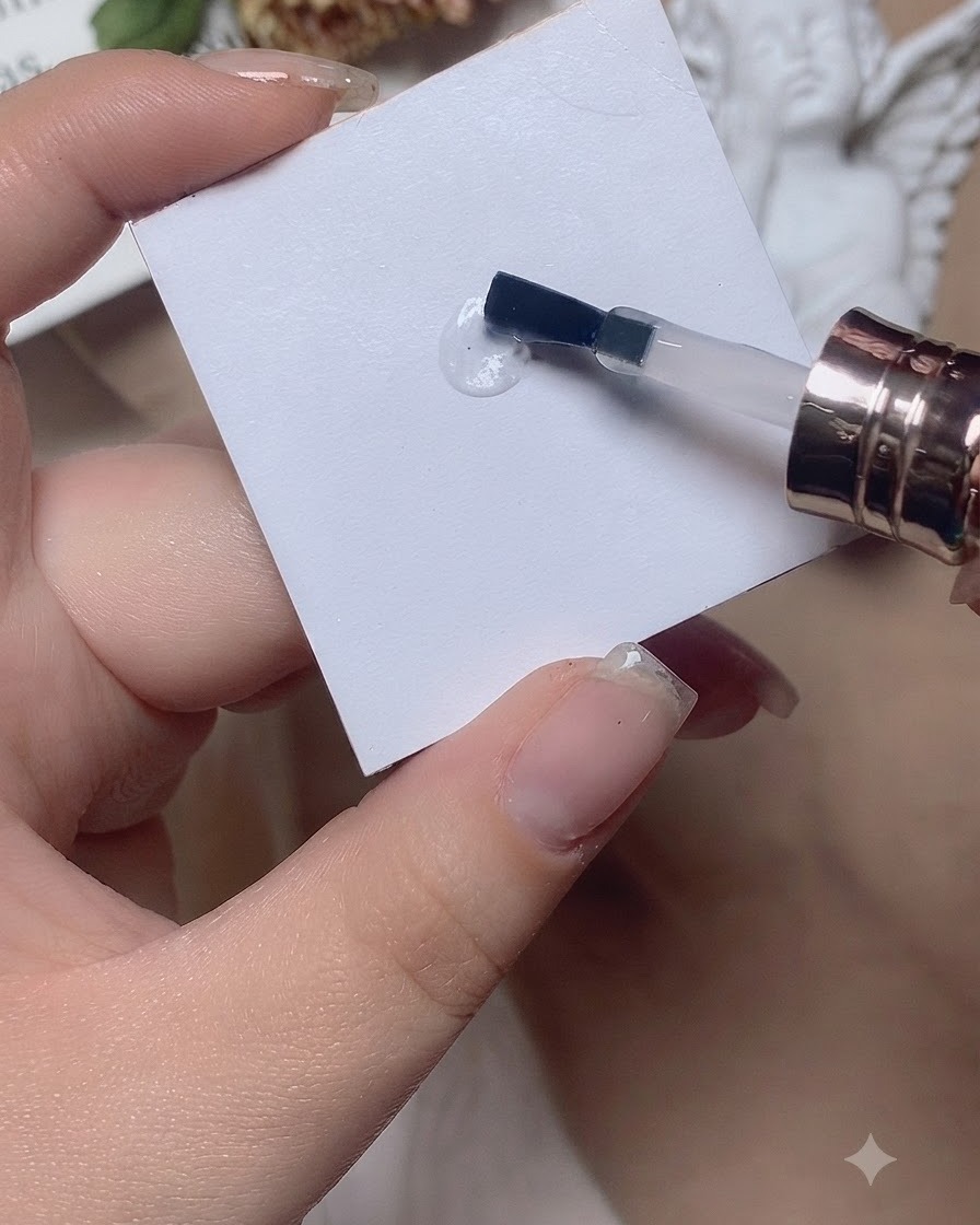 Ein Pinsel arbeitet einen Tropfen Base Coat auf einer weißen Palettenoberfläche hin und her.