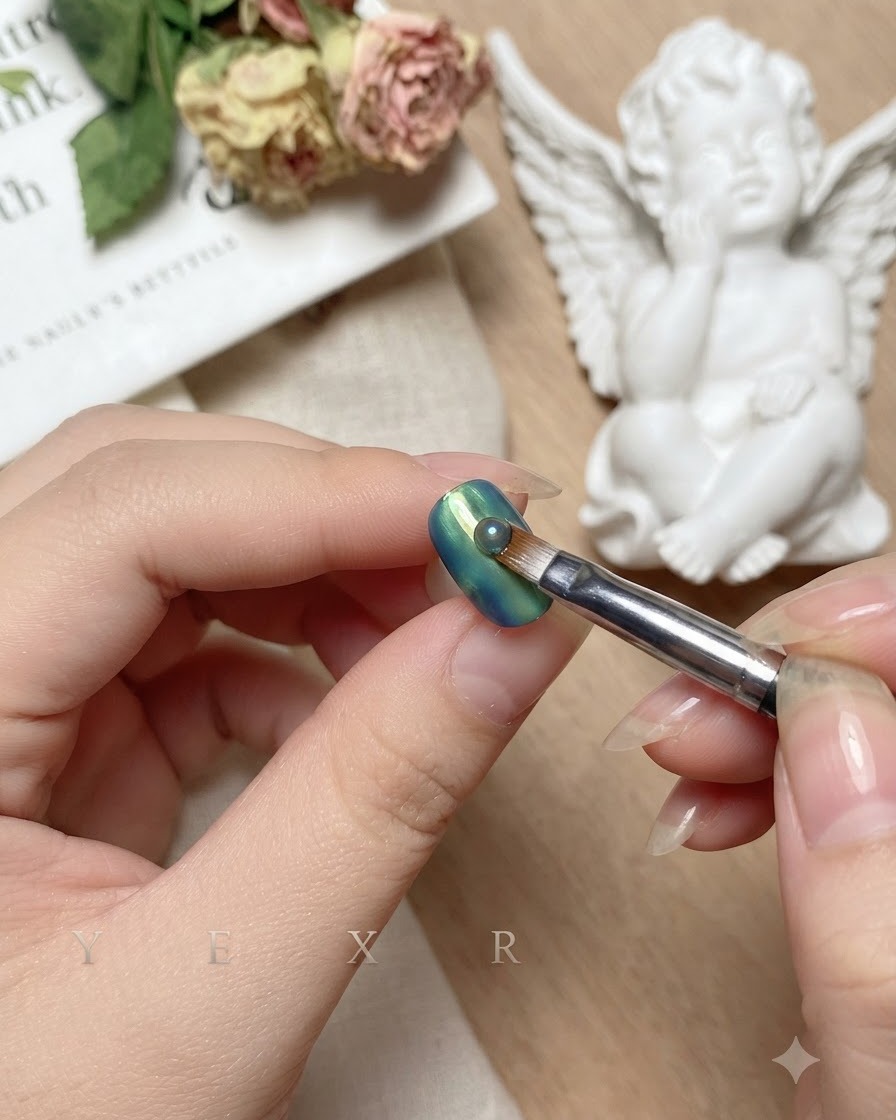Ein Pinsel zieht vertikal nach unten in die Mitte des verblendeten blauen und grünen Nagels.