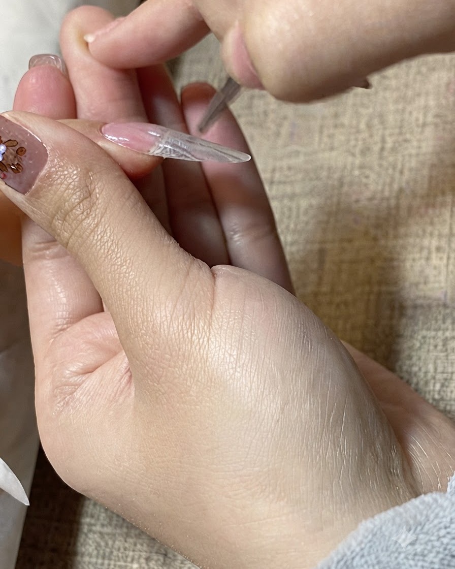 Nahaufnahme eines Detailpinsels, der klares Gel über die Oberfläche einer Nagelverlängerung glättet.cite: 1
