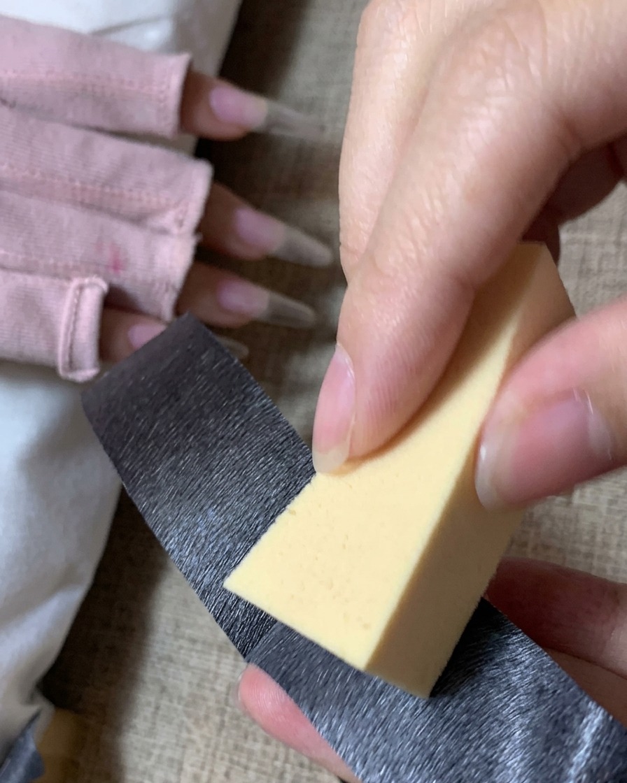 Eine Person entfernt mit schwarzem Klebeband Staub von einem dreieckigen gelben Make-up-Schwamm.cite: 1