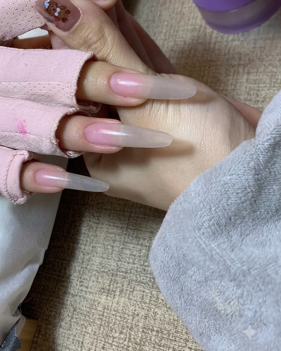 Eine Hand hält die Hand einer Kundin und zeigt einen weichen Nude-Farbverlauf, der mit einem Schwamm auf die Nagelverlängerungen aufgetragen wurde.cite: 1