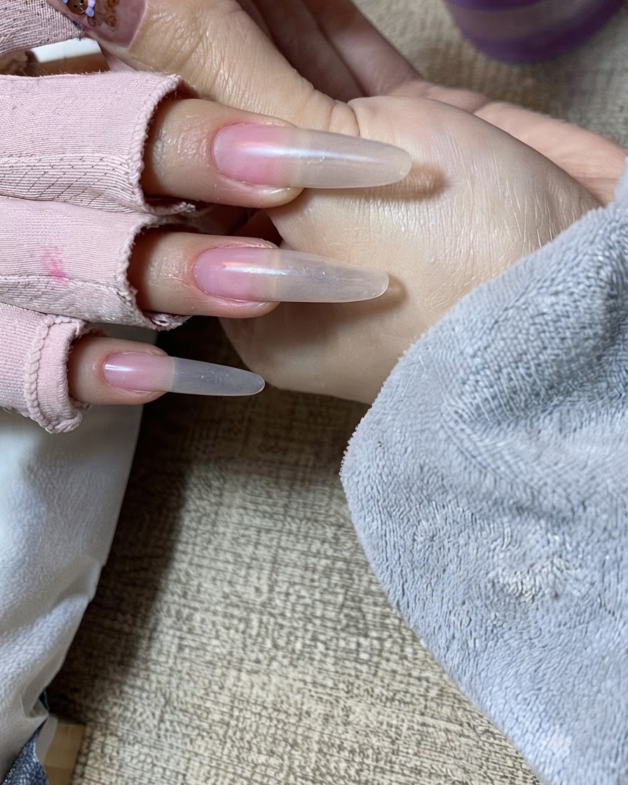 Nahaufnahme einer Hand, bei der die zweite Schicht Nude-Gel vorsichtig auf die freie Nagelkante aufgetupft wird.cite: 1