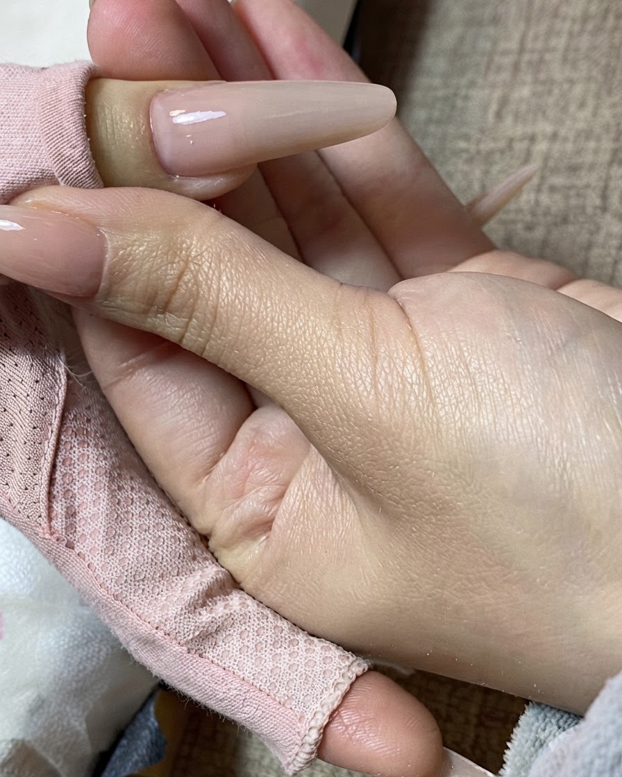 Nahaufnahme einer Hand, die einen fertig manikürten Nagel in Milchteefarbe hält.cite: 1