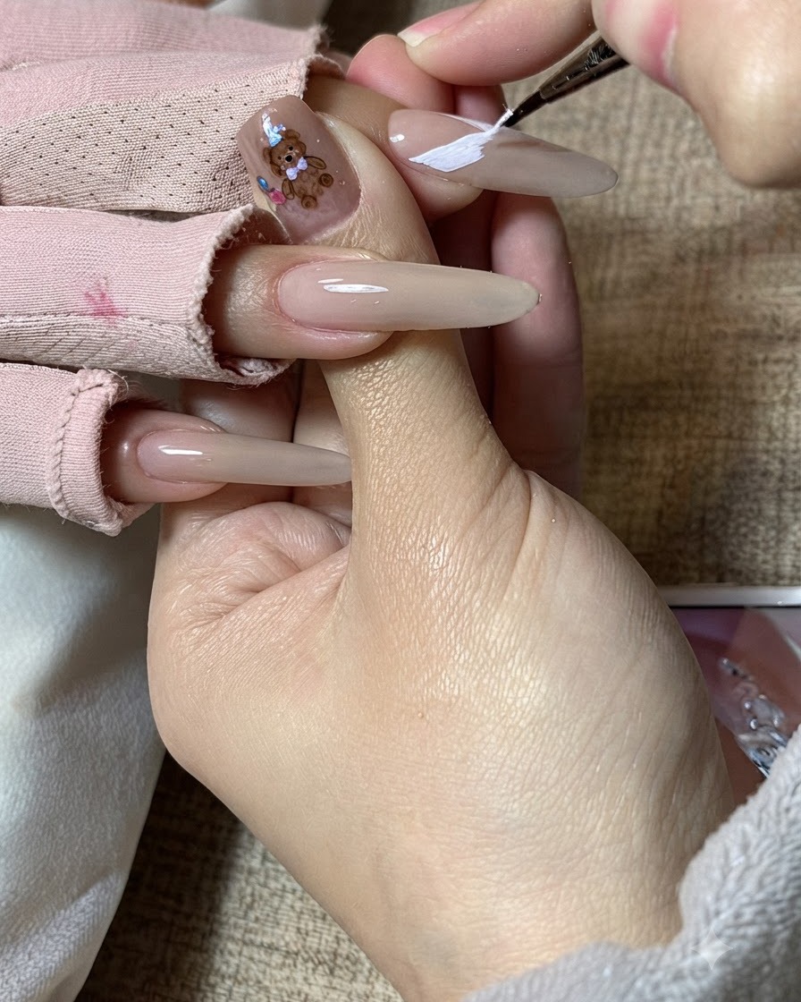 Die Hand einer Nageldesignerin verfeinert weiße Schmetterlingsflügelmuster auf einem langen Nagel.cite: 1