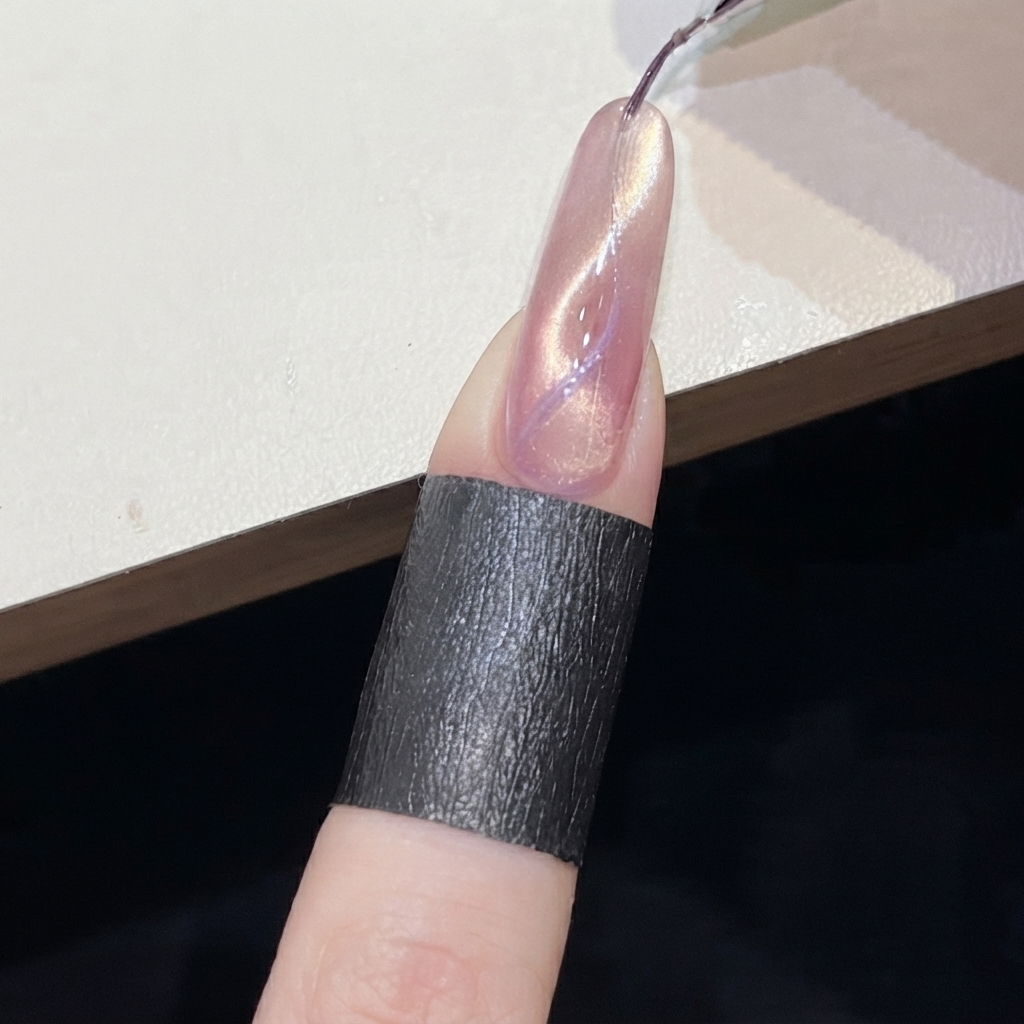 Ein zylindrischer Magnet wird nahe an eine lila Cat-Eye-Linie auf einem rosa Nagel gehalten.