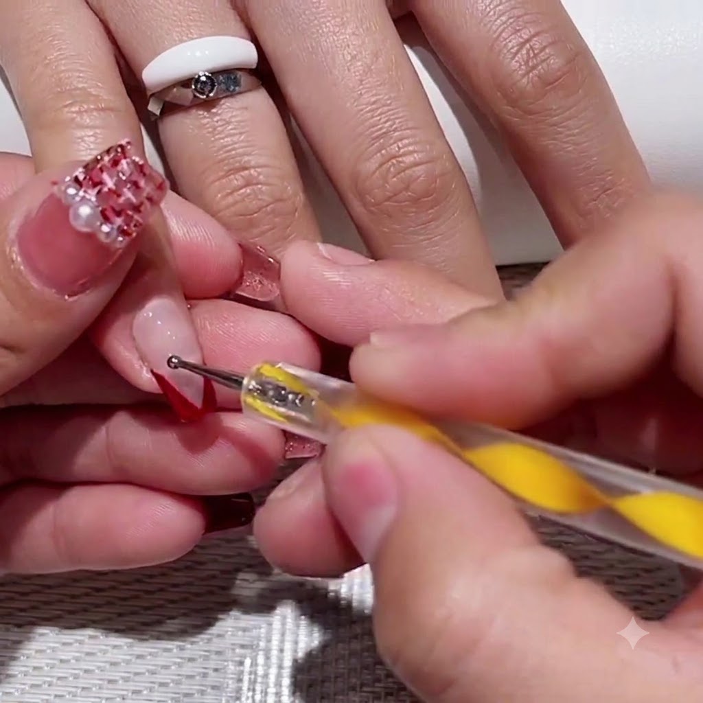 Ein Dotting-Tool mit gelbem Griff setzt zwei kleine rote Punkte in den klaren Negative-Space-Bereich eines V-Tip-Nagels.