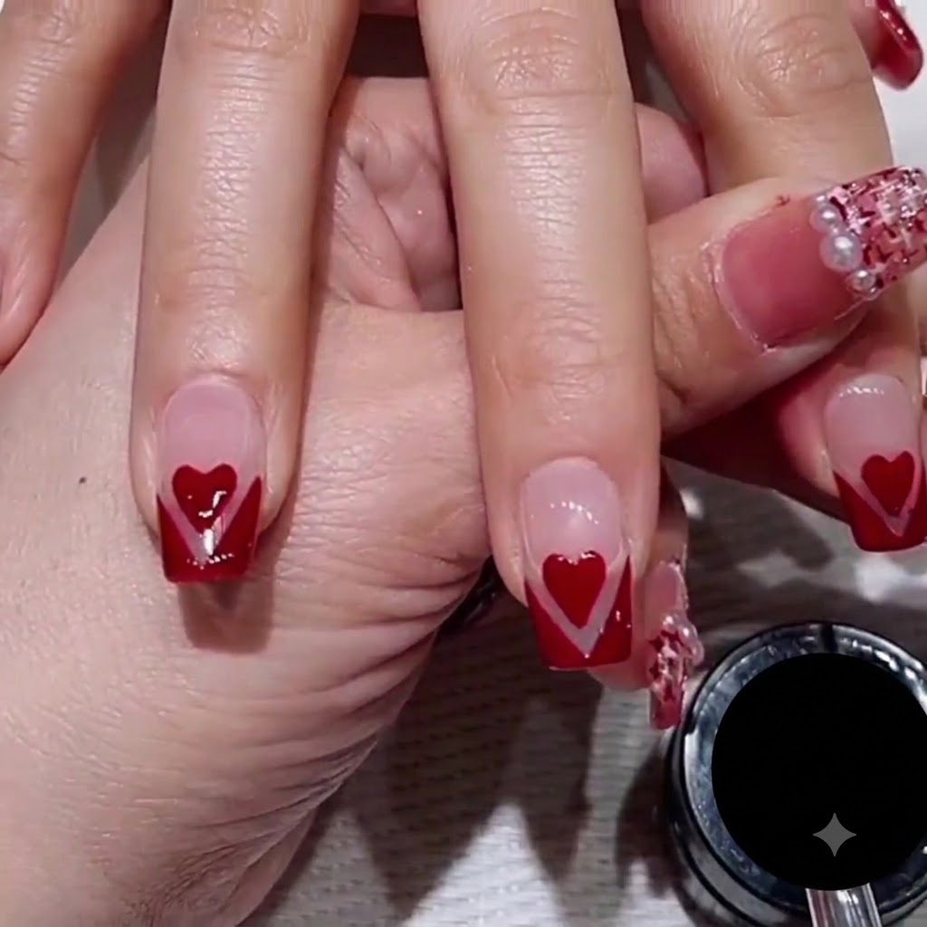 Nahaufnahme der Hand eines Nageldesigners, die einen dünnen Striper-Pinsel verwendet, um eine feine roségoldene Glitzerlinie entlang der Kante eines roten V-Tip-Nageldesigns zu ziehen.