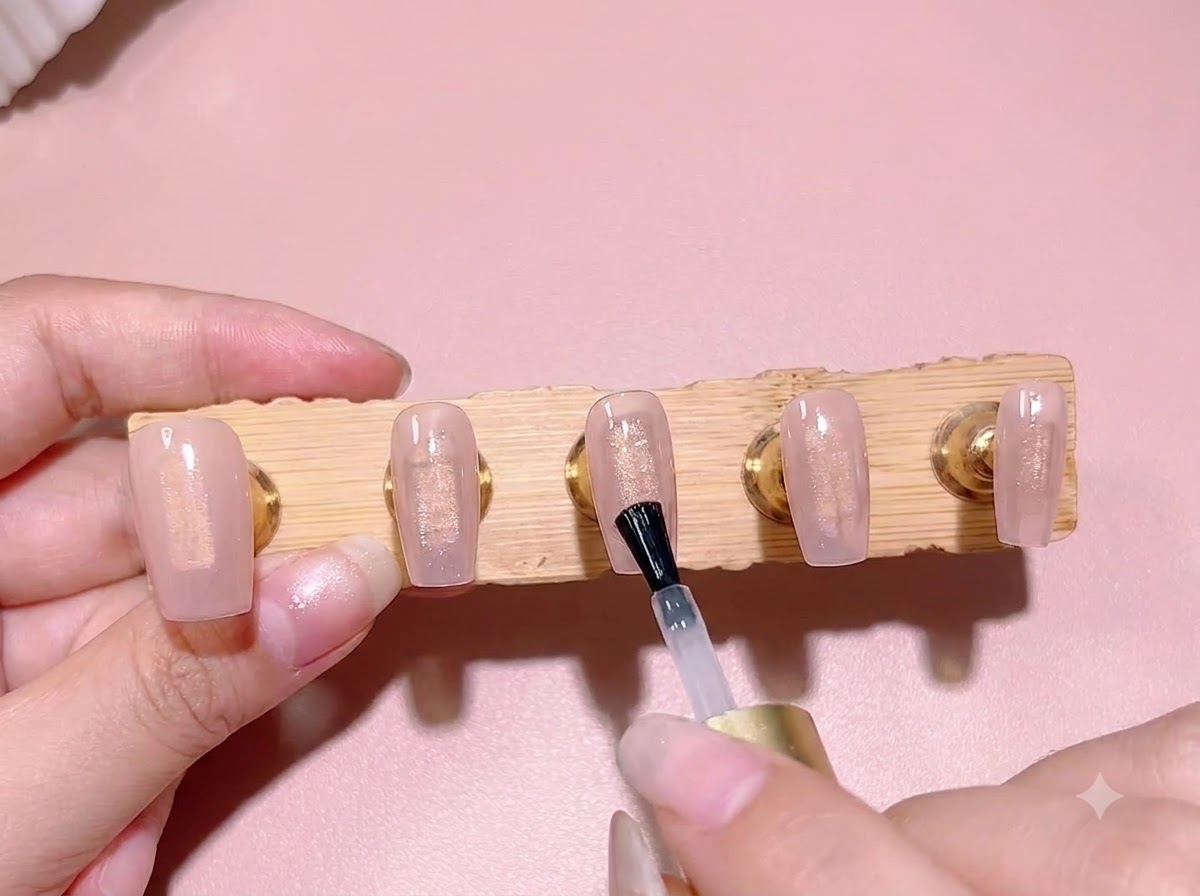 Ein Standard-Nagellackpinsel trägt eine Schicht klares Blooming Gel über einer transparenten rosa Basisfarbe auf eine Nagelspitze auf.