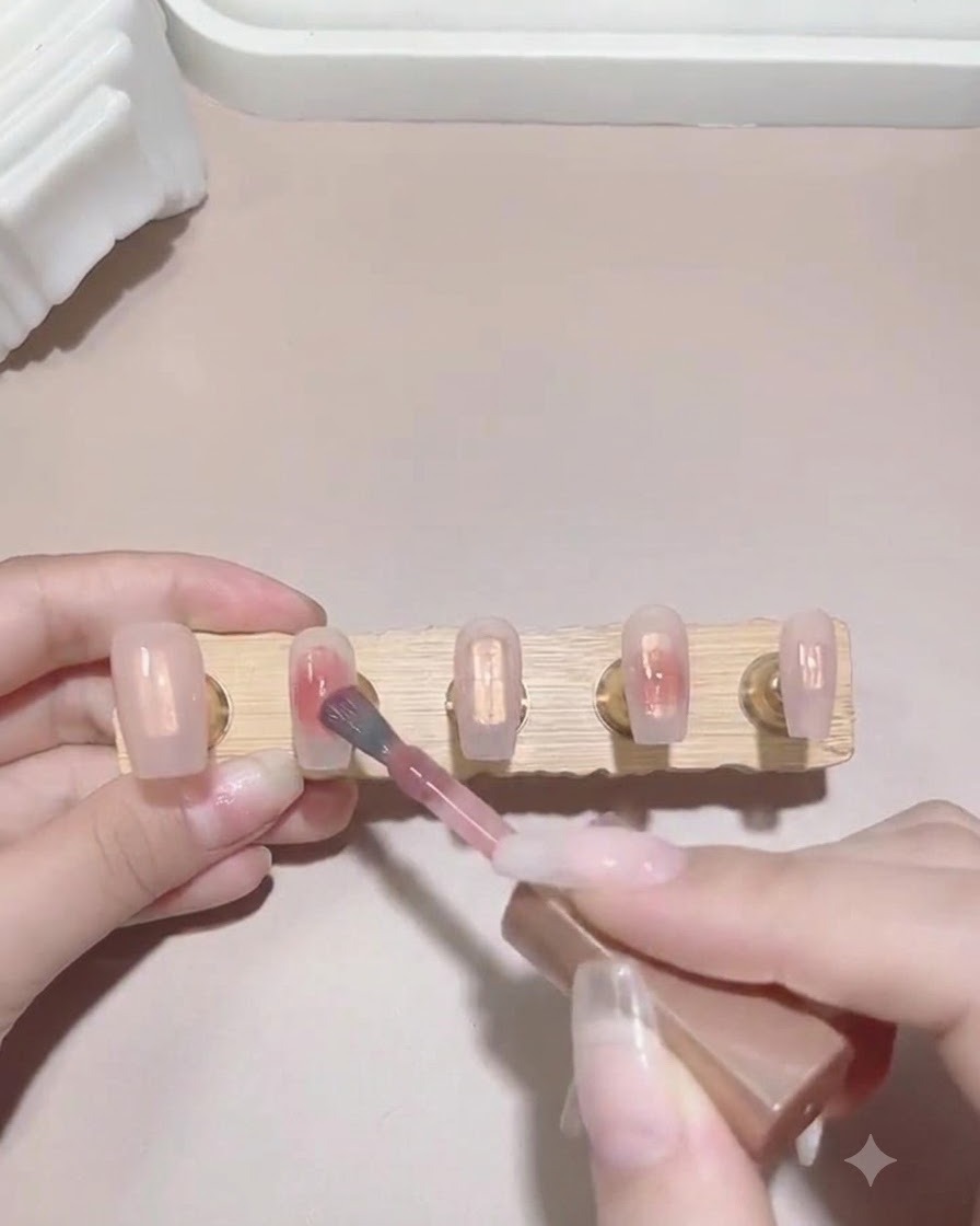 Ein Pinsel tupft einen kleinen Tropfen rosa Gel-Polish auf die feuchte Oberfläche einer Nagelspitze, um einen Verlaufseffekt zu beginnen.