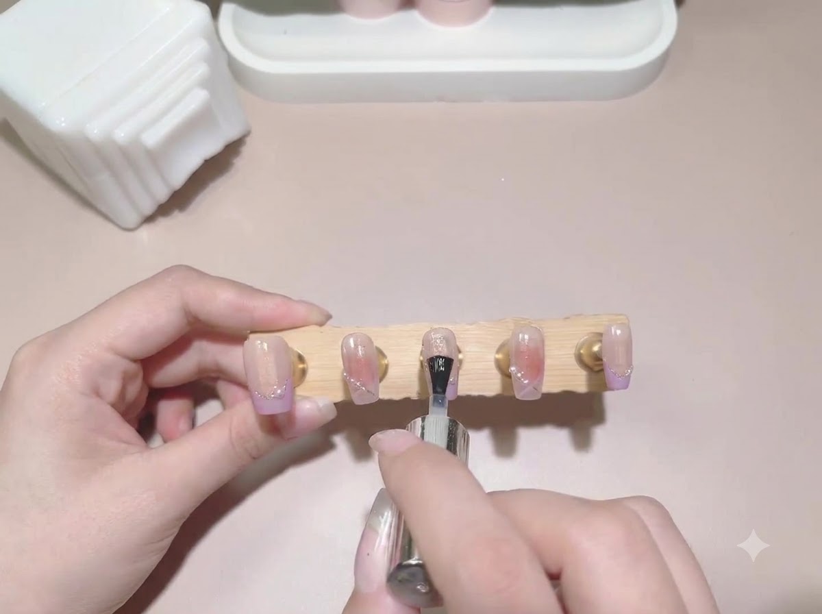 Ein Top-Coat-Pinsel wird über einen Display-Ständer mit fertig bemalten falschen Nägeln gezogen.