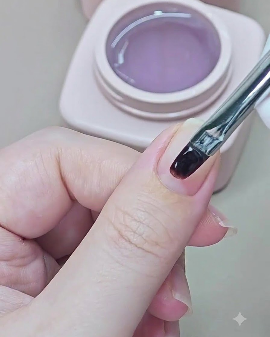 Ein kleiner Pinsel trägt klares Base Gel auf einen natürlichen Fingernagel auf.