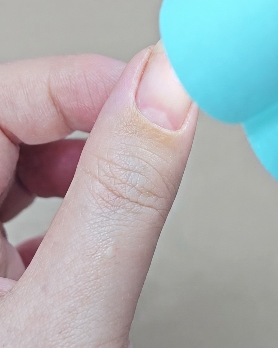 Eine kleine blaue UV-Handlampe wird direkt über einem Finger positioniert, um den Base Coat auszuhärten.