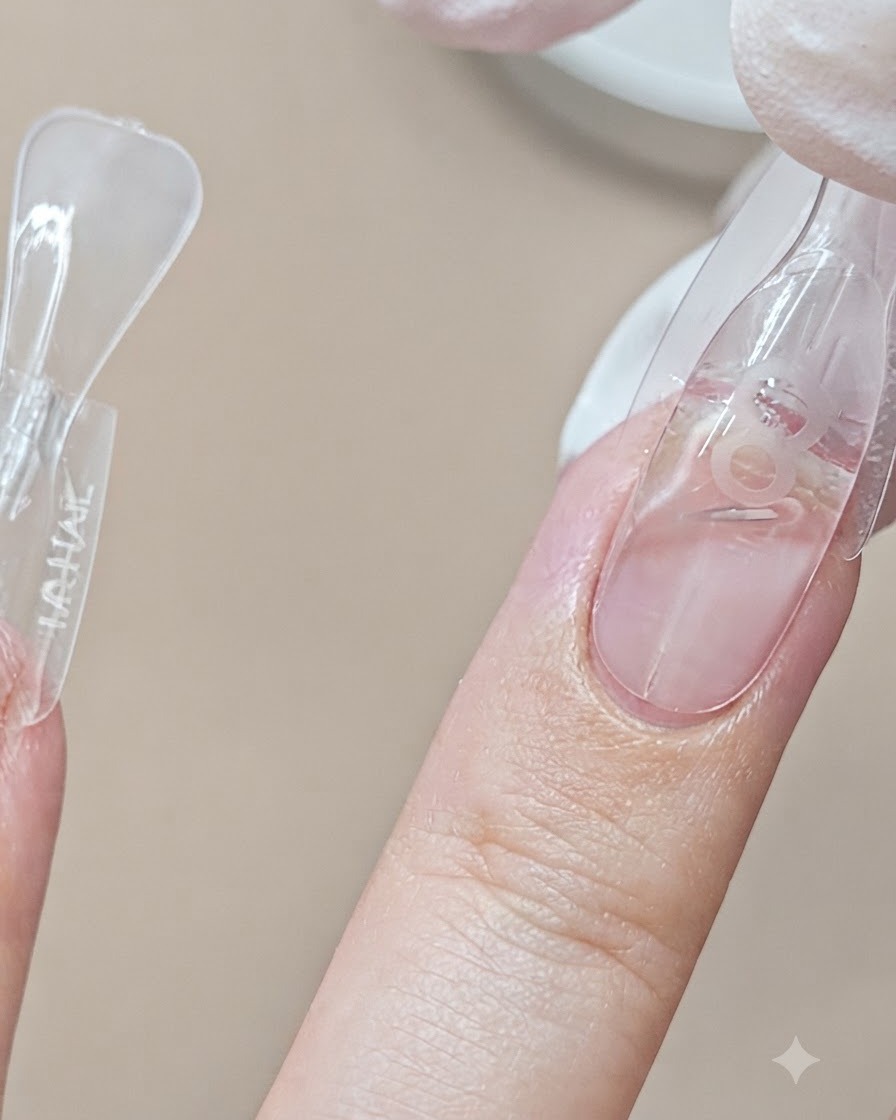 Eine Dual-Form-Schablone wird neben einem anderen fertigen Finger auf einen Mittelfingernagel aufgesetzt.