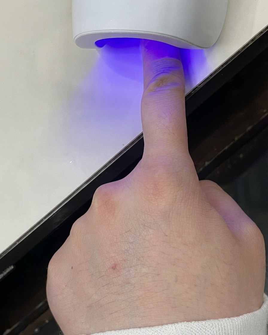 Ein Finger unter einer Mini-UV-LED-Lampe, die die Gelschicht aushärtet.