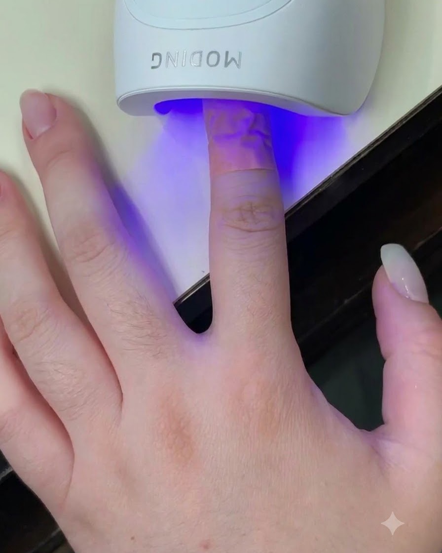 Ein Finger in einer weißen Mini-UV-LED-Lampe, während ein blauer Lichtschein auf den Nagel strahlt.