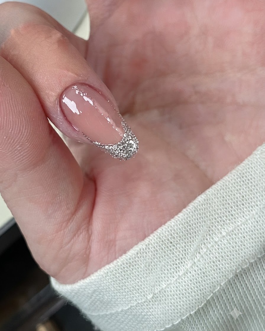 Eine Nahaufnahme eines Fingernagels mit dicht aufgetragener, grober Silberglitter-Schicht über der French-Spitze.
