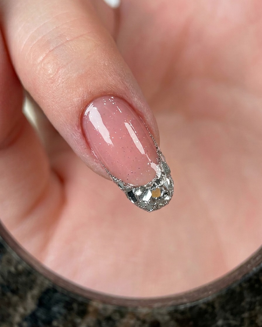 Eine Nahaufnahme eines Fingers mit einer French-Spitze, die über einer rosa Basis dicht mit grobem Silberglitter gefüllt ist.