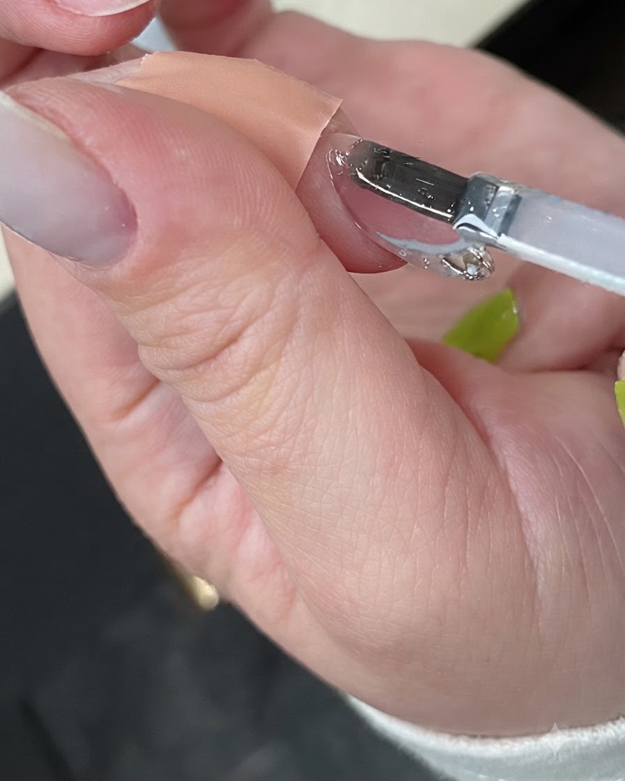 Eine Hand härtet die fertige Maniküre in einer kompakten weißen UV-Nagellampe aus.