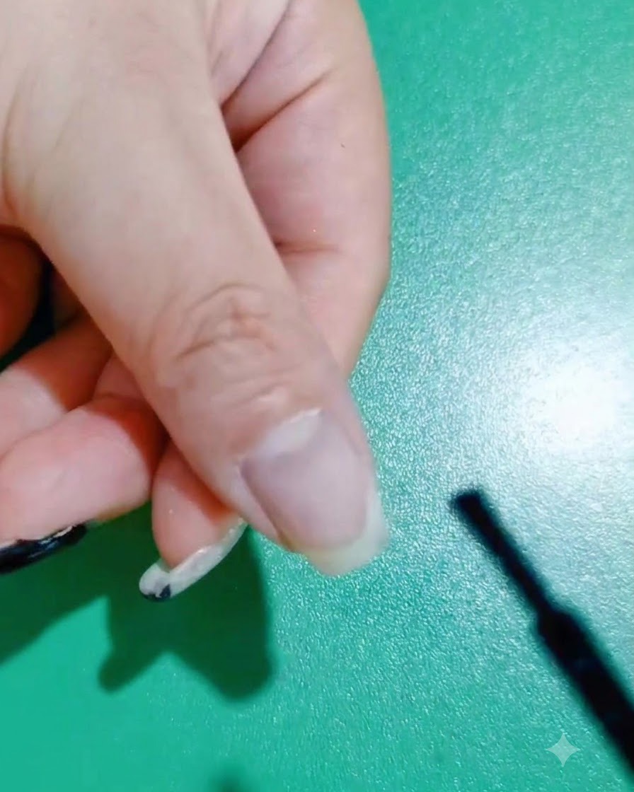 Ein Nagelpinsel trägt eine erste Schicht schwarzen Gel-Lacks auf einen Naturnagel auf.
