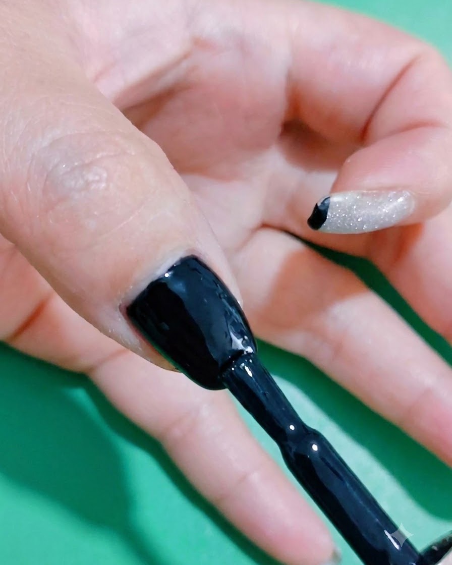 Ein Nagelpinsel trägt eine zusätzliche Schicht schwarzen Gel-Lacks auf, um eine satte Farbsättigung zu gewährleisten.