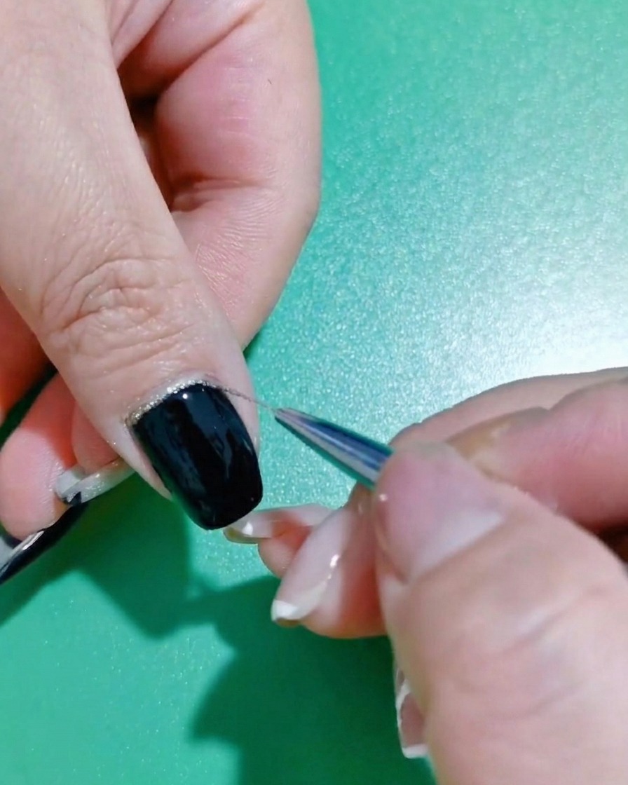 Eine Nahaufnahme eines feinen Liner-Pinsels, der Glitzerlack am Rand eines schwarzen Nagels verfeinert.