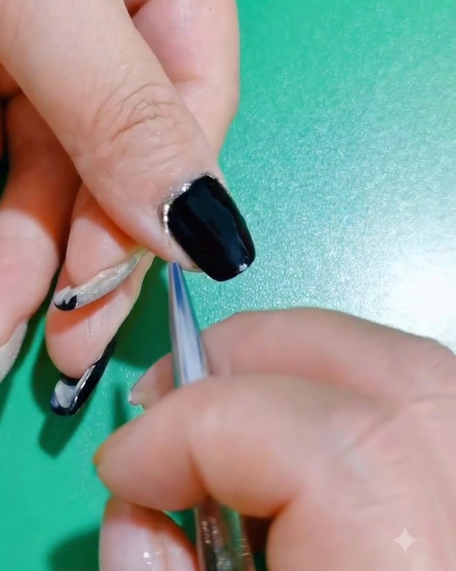 Eine Nahaufnahme zur Überprüfung eines fertigen Nageldesigns in Schwarz und Glitzer.