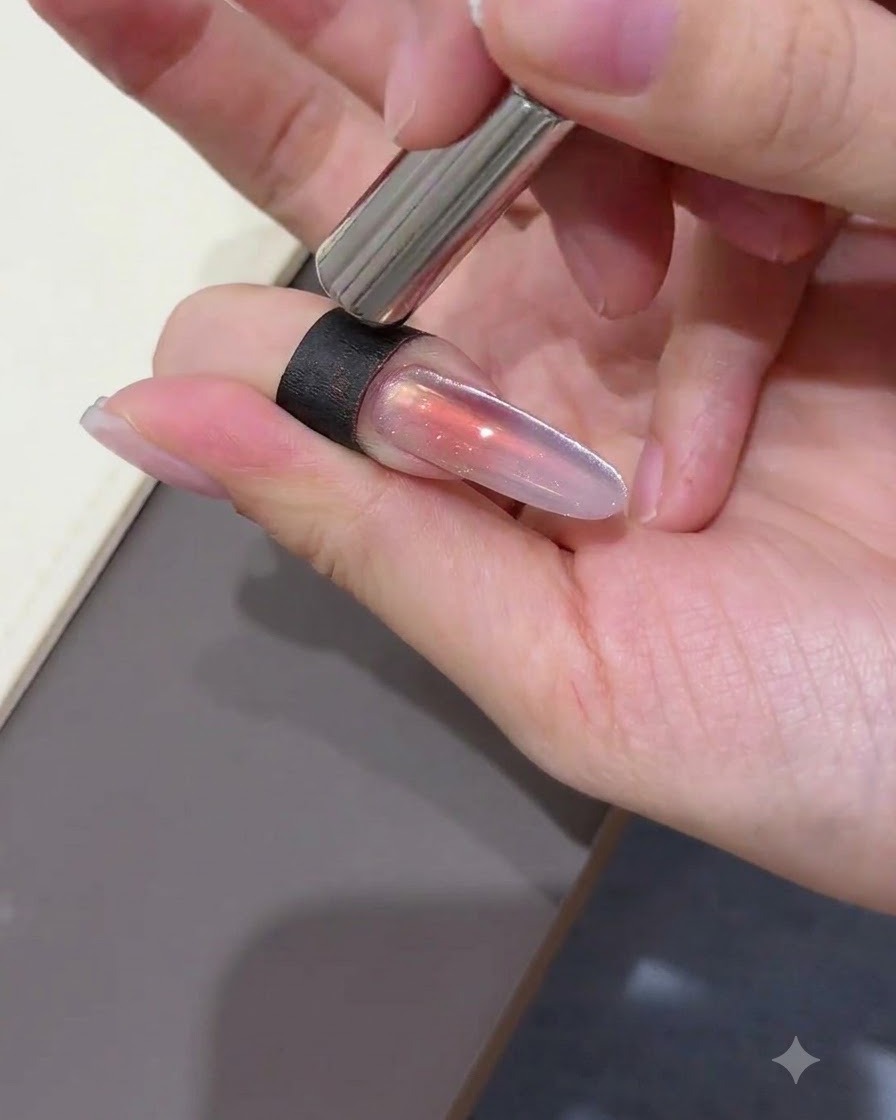 Ein zylindrischer Magnet wird dicht an die rechte Seite eines langen mandelförmigen Nagels gehalten, um Cat-Eye-Gel-Partikel zu einer hellen Randreflexion zu ziehen.