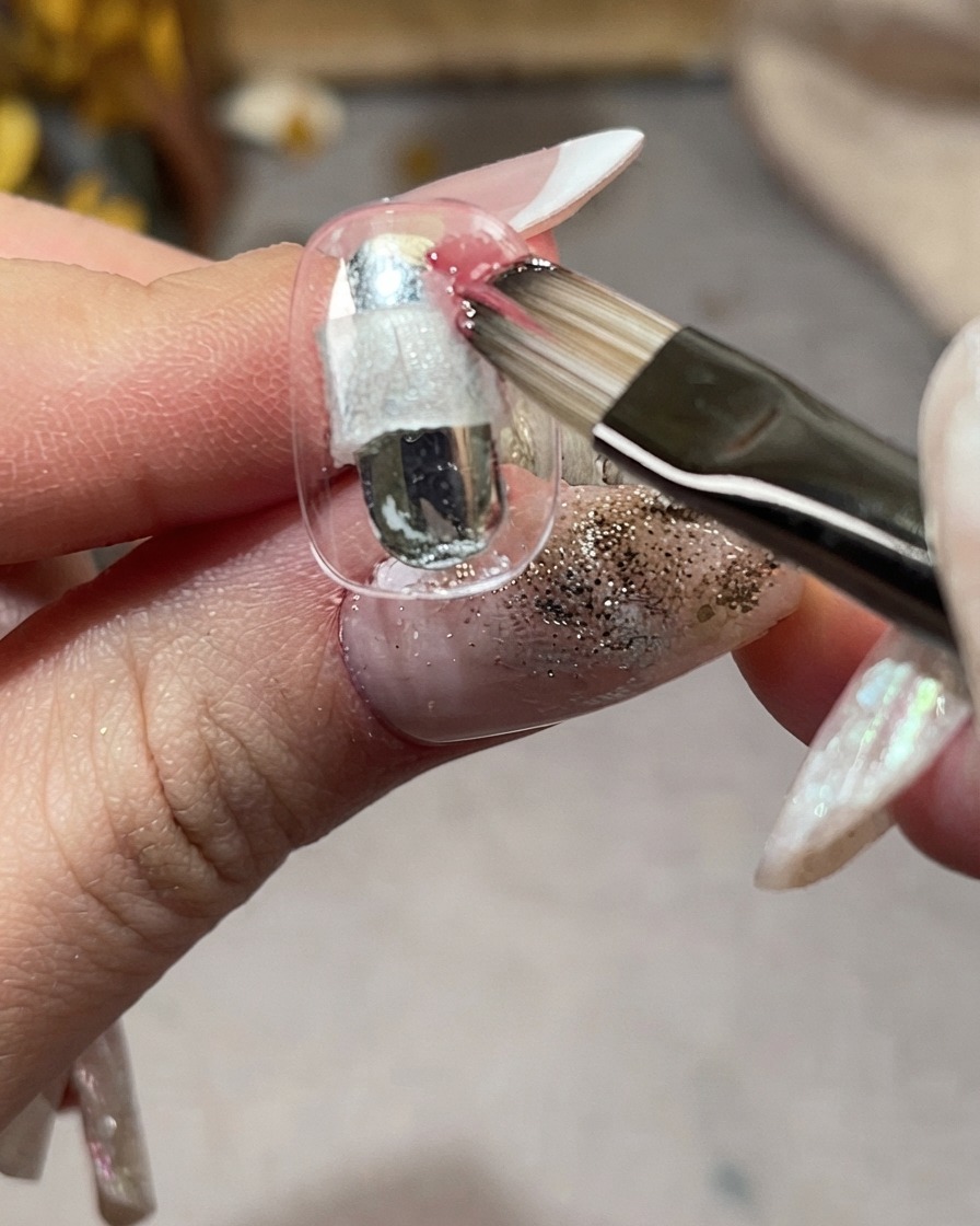 Ein Pinsel trägt rosa Gel diagonal auf einen klaren Nagel-Tip auf.