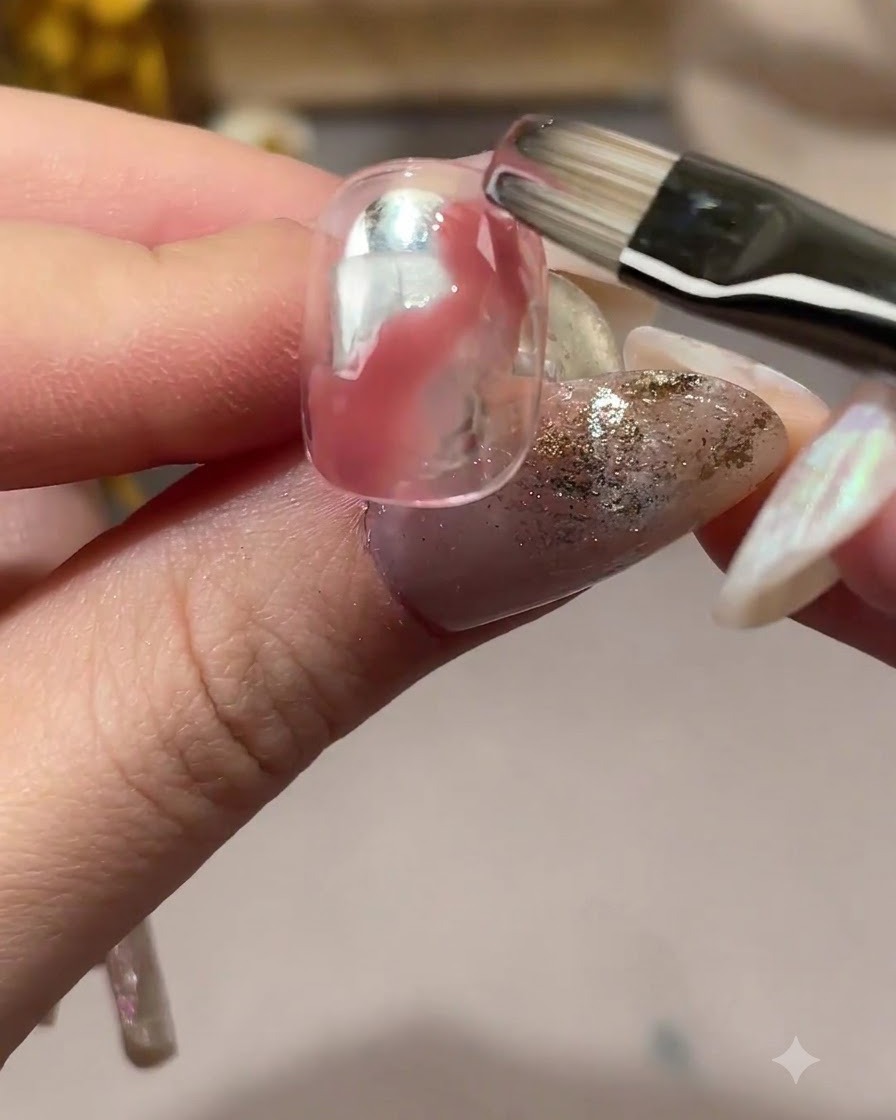 Ein Nagelpinsel verblendet die Kanten des rosa Gels auf einer klaren Nageloberfläche.
