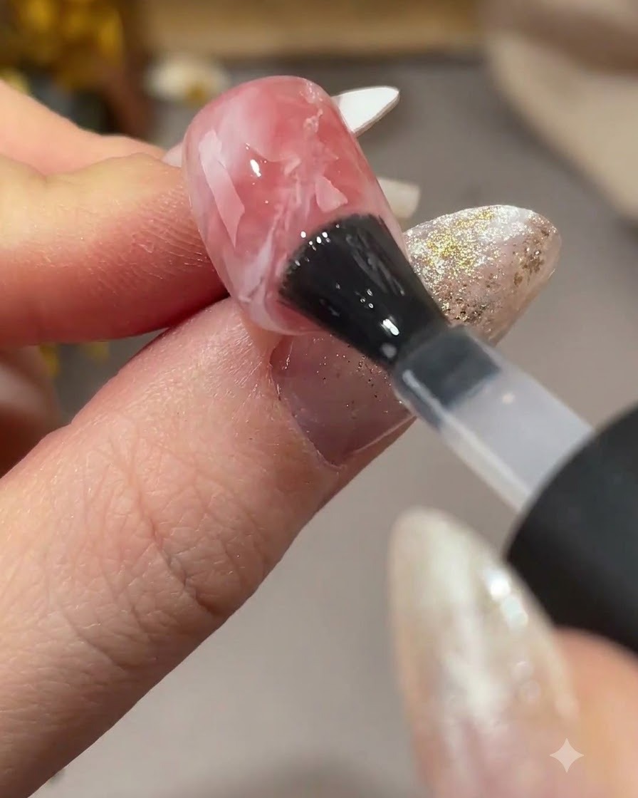 Ein Pinsel trägt matten Topcoat über ein strukturiertes rosa-weißes Nageldesign auf.