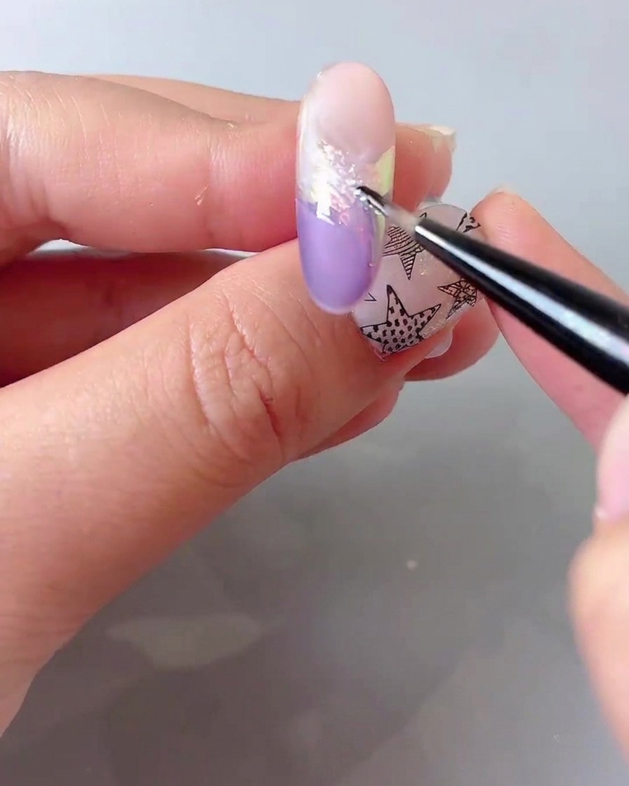 Ein feiner Detailpinsel, der feines holografisches Glitzerpuder über einen Nagel streut.