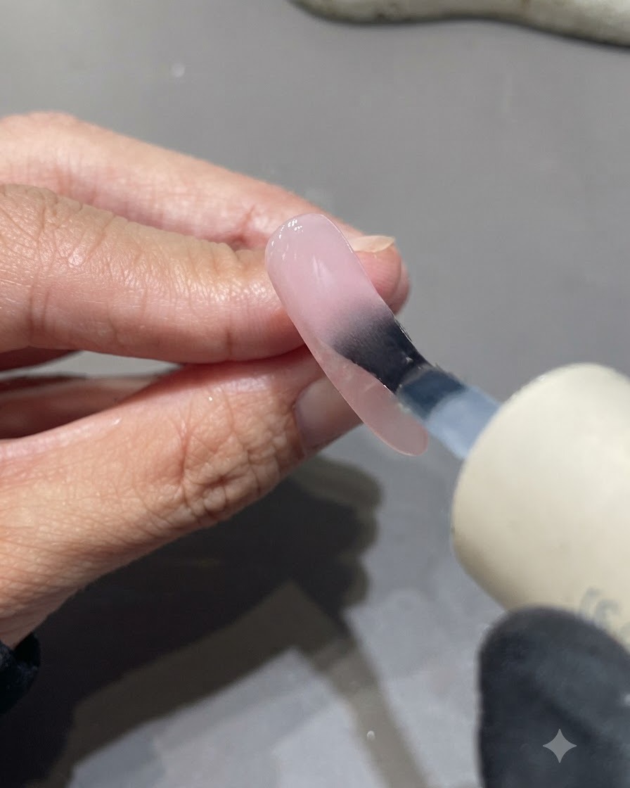 Ein Pinsel trägt matten Topcoat über eine rosa getönte Nageloberfläche auf.