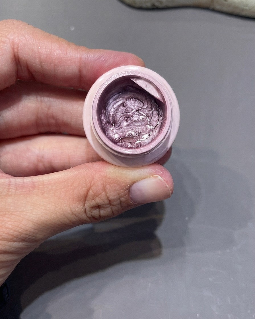 Eine Hand hält ein offenes Gefäß mit silber-violettem Cat-Eye-Gel, während ein feiner Liner-Pinsel hineingetaucht wird.