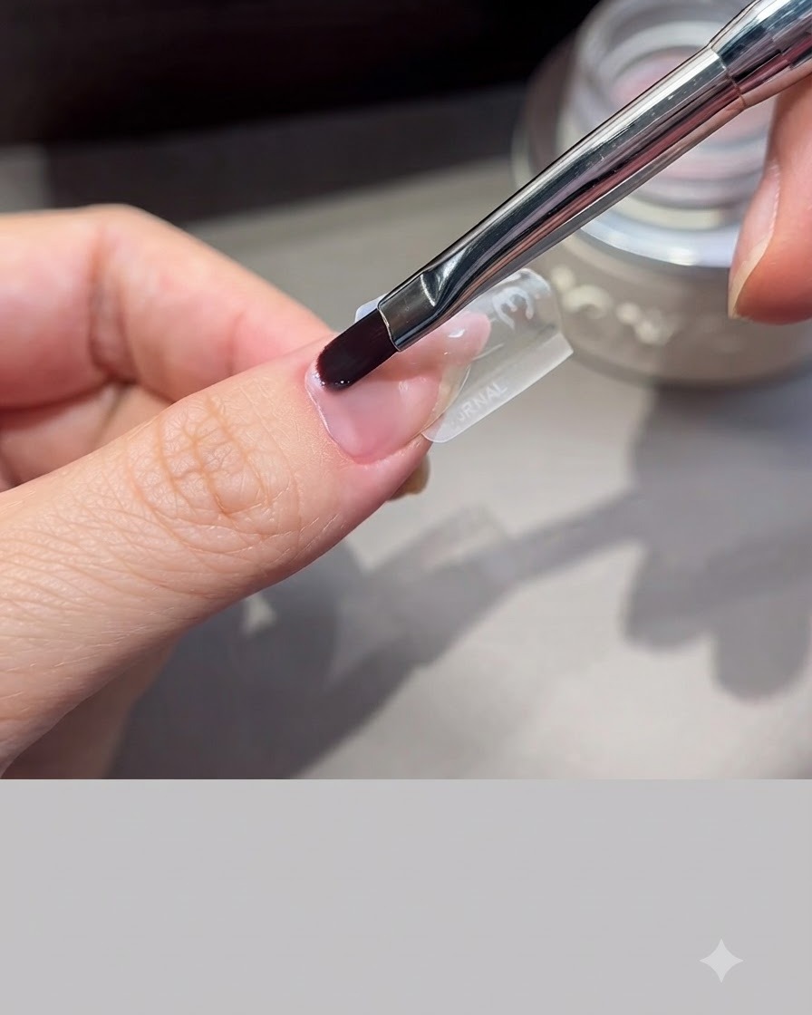 Ein professioneller Nagelpinsel glättet Verlängerungsgel über einer klaren Nagelschablone auf einem Finger.