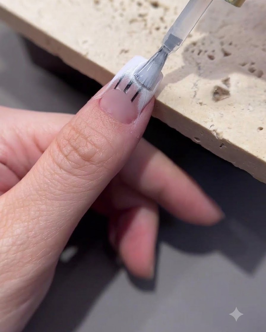 Ein Pinsel trägt Transfergel auf den Spitzenbereich eines verzierten Nagels auf.