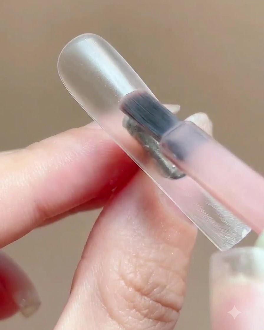 Ein Pinsel trägt eine dünne Schicht durchsichtiges rosa Gel-Nagellack auf einen klaren Nagel-Display-Ständer auf.