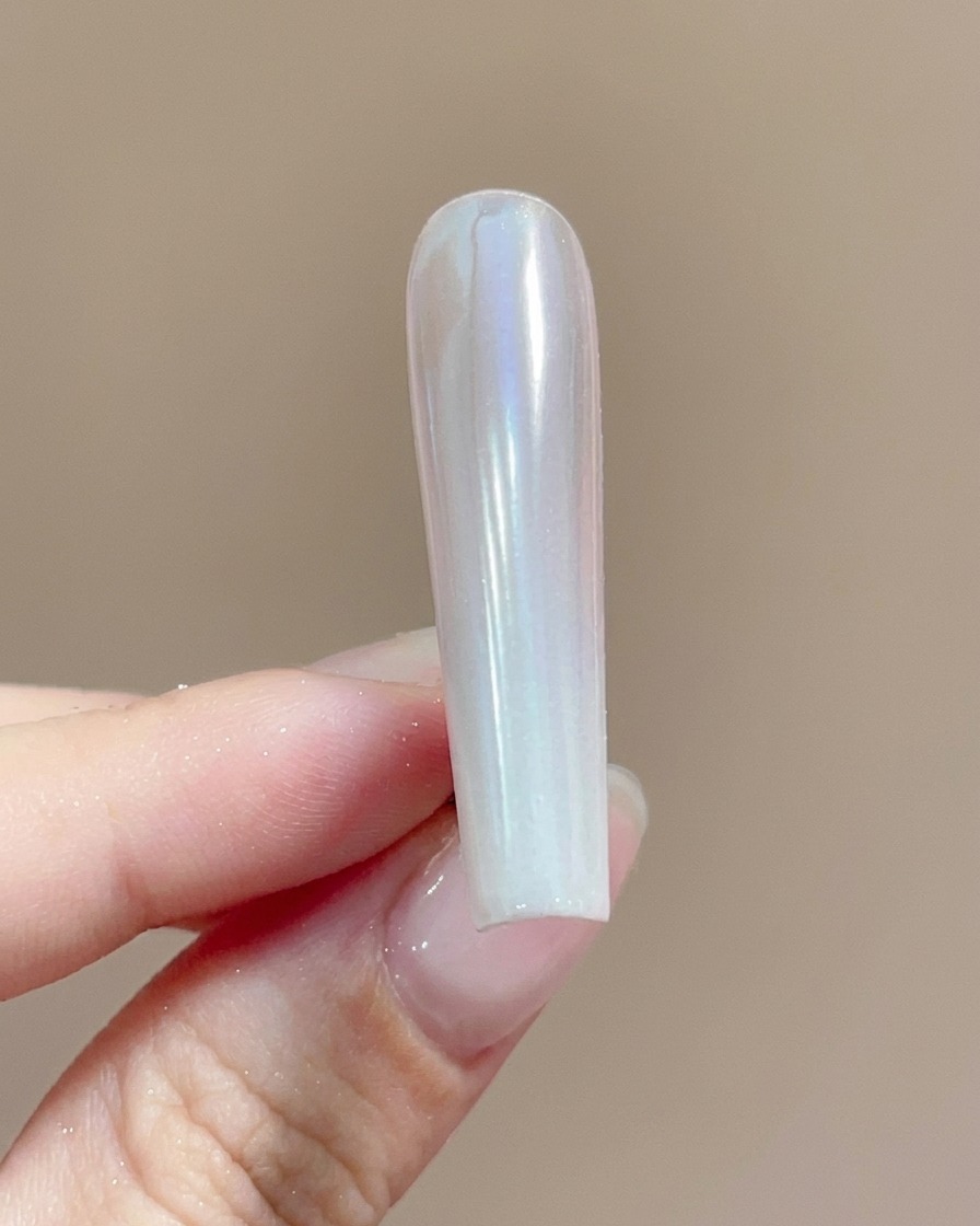 Ein Pinsel trägt einen klaren Top Coat über einen mit schimmerndem Chrompulver beschichteten Nagel auf.