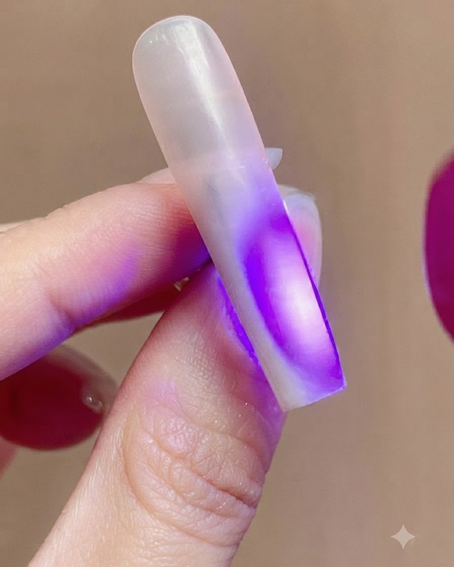 Ein Fingernagel, der während des Aushärtungsprozesses durch violettes UV-Licht einer Nagellampe beleuchtet wird.
