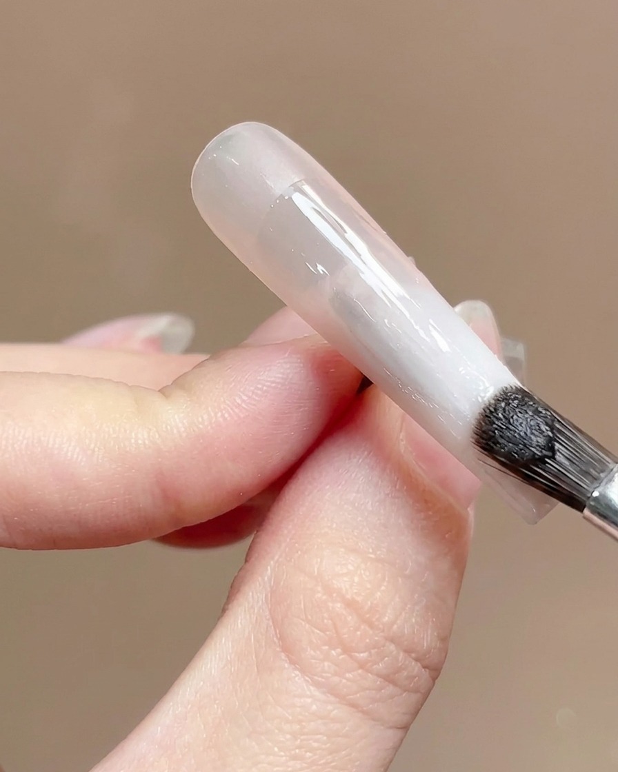 Ein Nagelpinsel trägt einen klaren, glänzenden Top Coat über eine Gradienten-Nageloberfläche auf.
