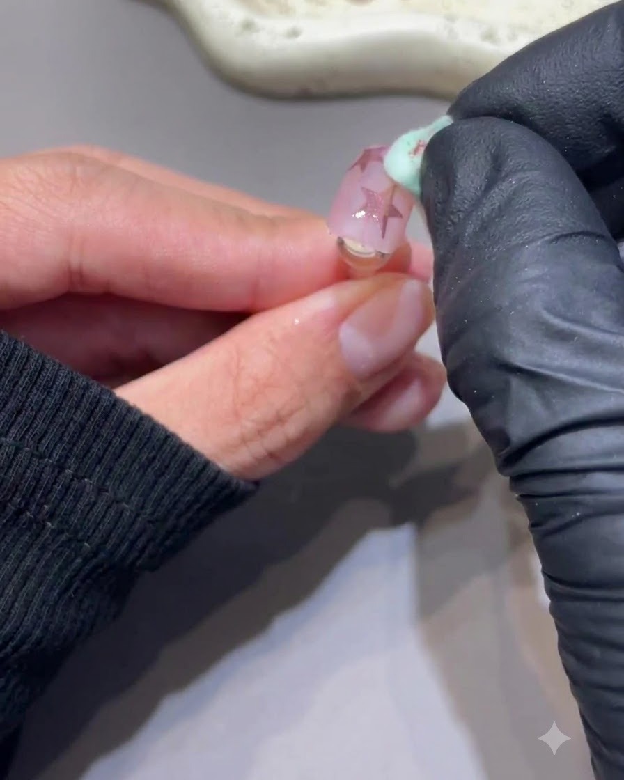 Ein sauberer Schwamm wischt überschüssiges Puder sanft von einem Nagel mit rosa Chromsternen ab.