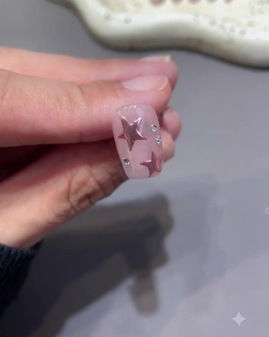 Ein winziger Detailpinsel zieht sorgfältig Top-Coat-Linien um die Basis kleiner Strasssteine auf einem fertigen rosa Sternennagel.