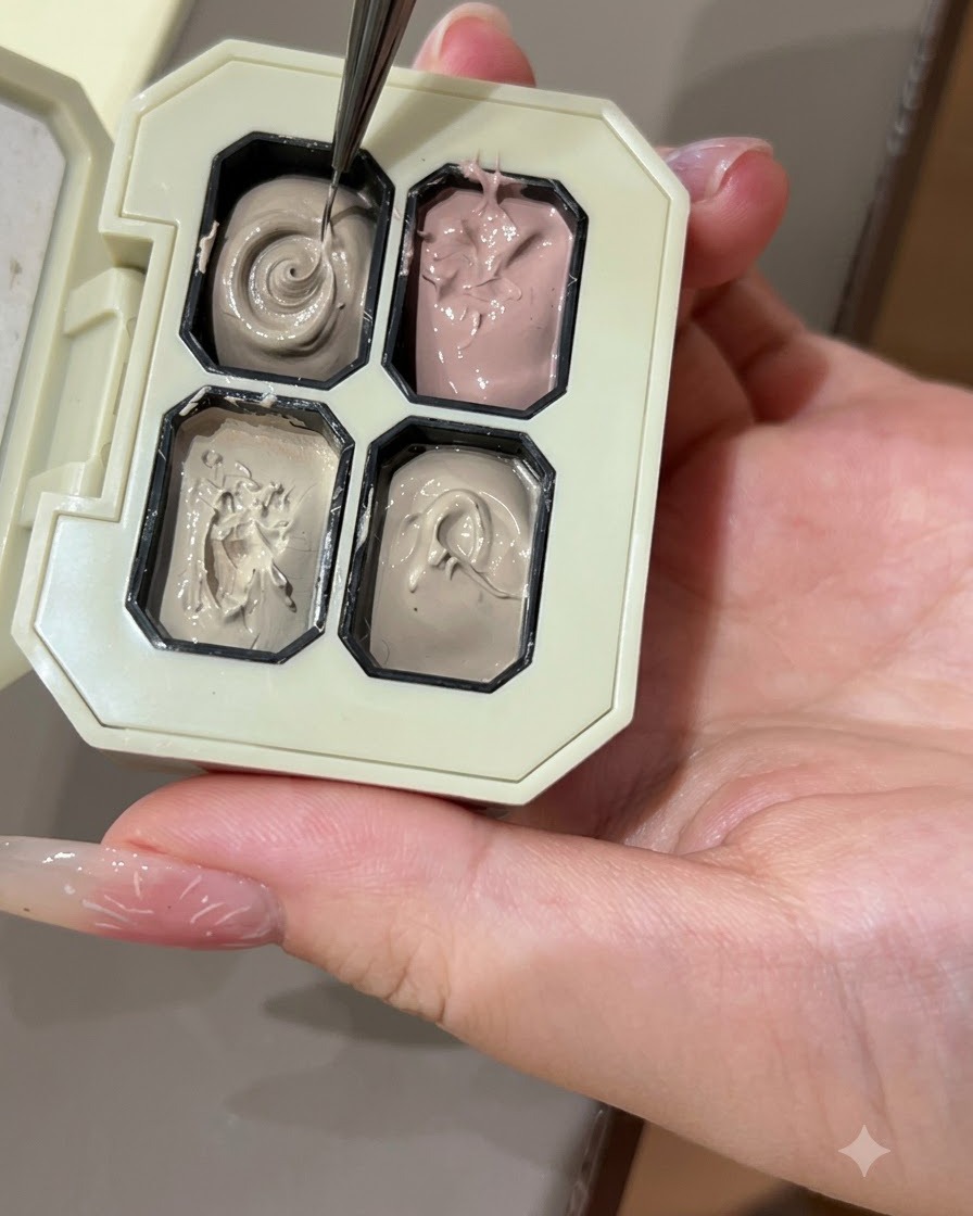 Ein feiner Nail-Art-Pinsel nimmt graues Farbgel aus einem Fach einer Palette auf.