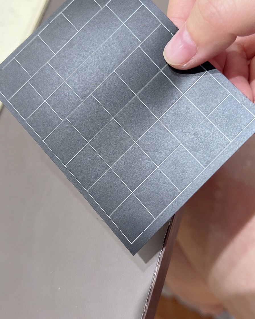 Eine Hand hält einen schwarzen Bogen mit rasterlinierten Nagelaufklebern und wählt einen Aufkleber aus.