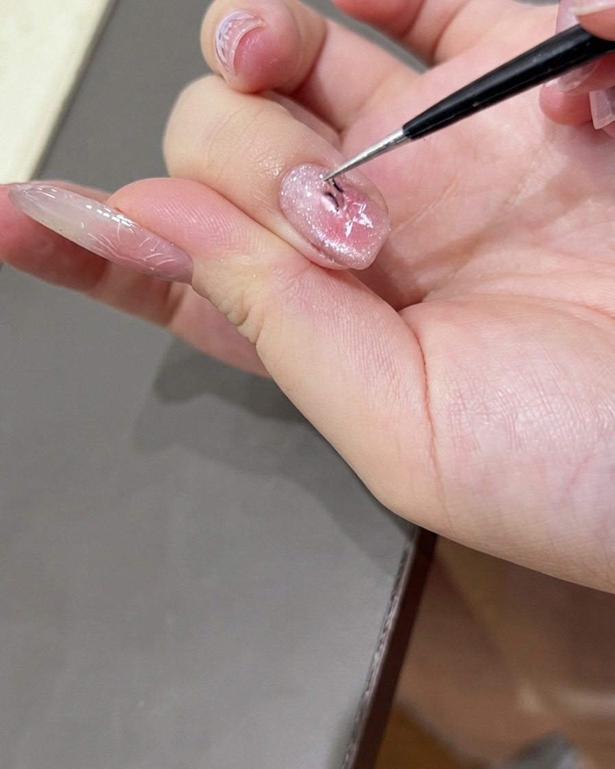 Eine feine Pinzette zieht vorsichtig einen sternförmigen Nagelaufkleber von einem lackierten Cat-Eye-Gel-Nagel ab.