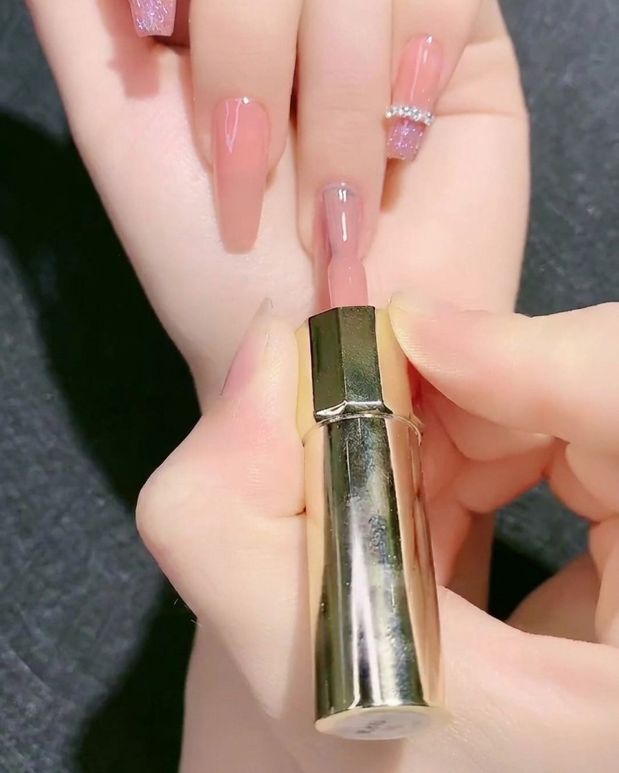 Ein Pinsel trägt Nude-Rosa Base-Gel auf einen Fingernagel auf.