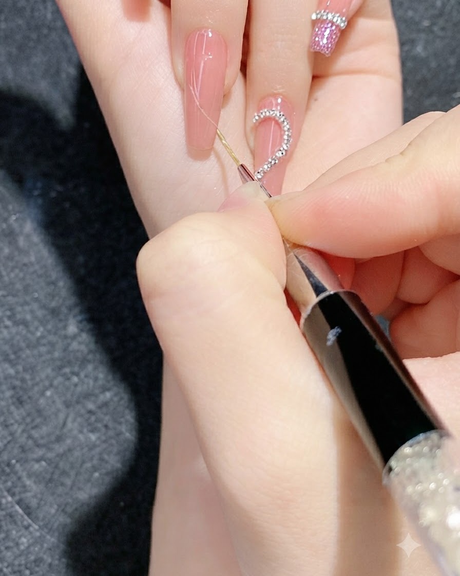 Eine Nahaufnahme einer detaillierten Nail-Art-Sitzung, bei der ein feines Werkzeug Strassketten-Streifen auf einen Gradienten-Nagel drückt.
